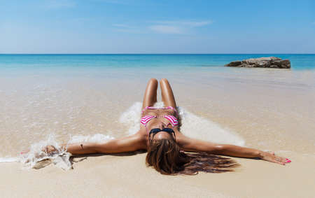 Young pretty slim brunette woman in sunglasses sunbathe on the tropical beach in bikiniの写真素材