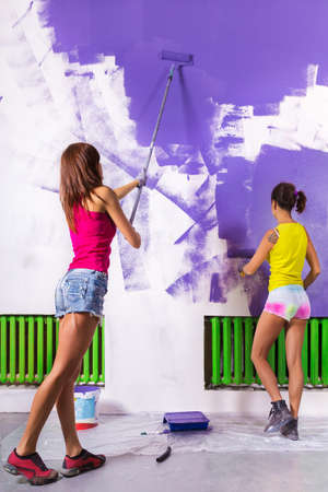 young beautiful women paints white wall and purple paint rollerの写真素材