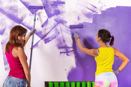 young beautiful women paints white wall and purple paint rollerの写真素材