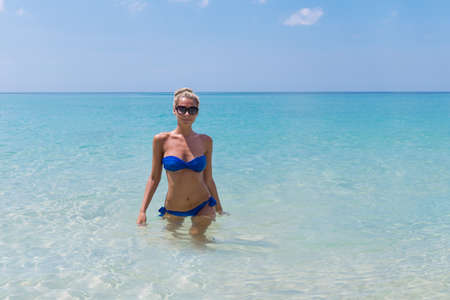 Young pretty slim blonde woman swimming in clear water on a tropic beach in bikiniの写真素材