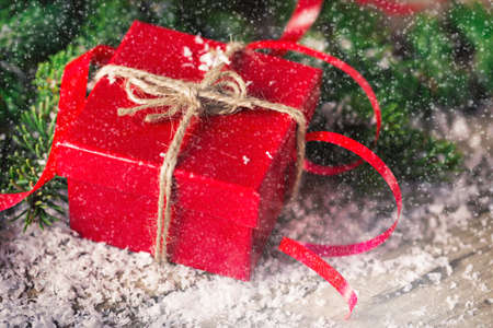 Red Christmas present box with fir and snow on wooden backgroundの写真素材