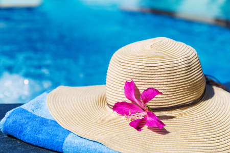 Straw hat with orchid flower and blue towel near swimming pool - holiday tropical conceptの写真素材