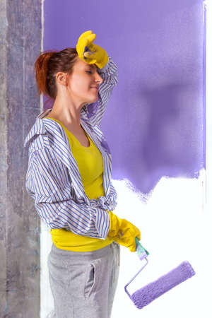 young attractive woman paints white wall and purple paint rollerの写真素材