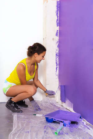 young attractive woman paints white wall and purple paint rollerの写真素材