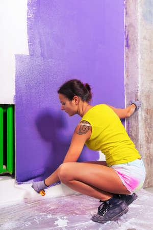 young attractive woman paints white wall and purple paint rollerの写真素材