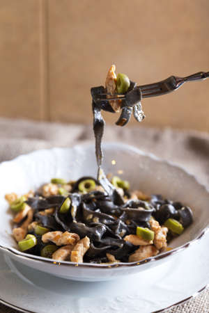 Black ink pasta with chicken and green olivesの写真素材