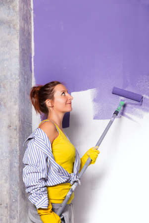 young attractive woman paints white wall and purple paint rollerの写真素材