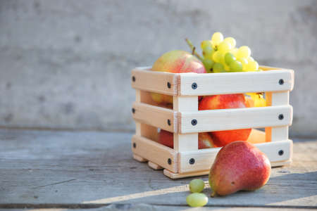 Grapes, pear and apple fruits in a box on wooden backgroundの写真素材