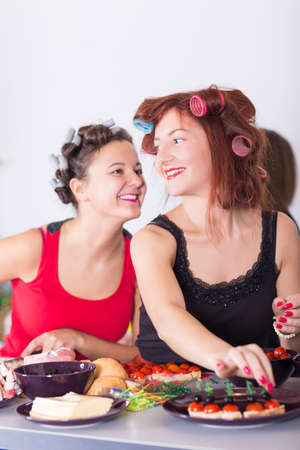 Two young pretty woman housewife cooking with curlers on hairの写真素材
