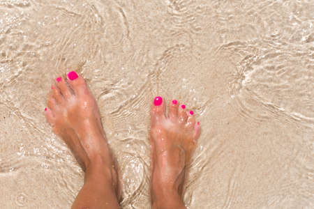 Woman legs stands in sea water on the tropic beachの写真素材