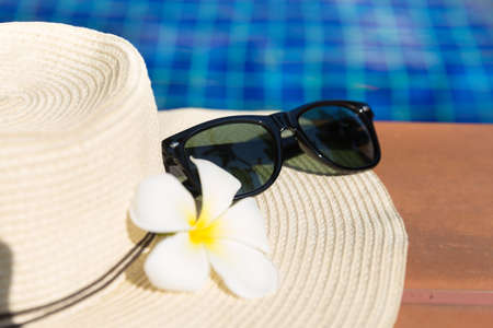Sunglasses with flower and straw hat on border of a swimming pool - holiday tropical conceptの写真素材