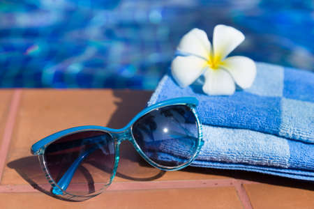 Fluffy towel with sunglasses and flower on border of a swimming pool - holiday tropical conceptの写真素材