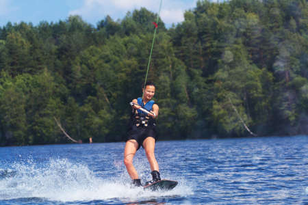 Young pretty slim brunette woman riding wakeboard on wave of motorboat in a summer lakeの写真素材