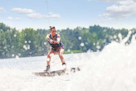 Young pretty slim brunette woman riding wakeboard on wave of motorboat in a summer lakeの写真素材