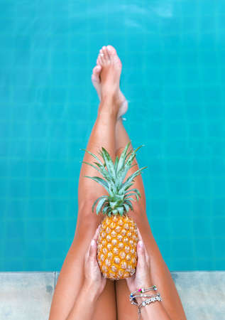 Slim woman holding pineapple fruit near swimming pool tropical exotic concept top viewの写真素材