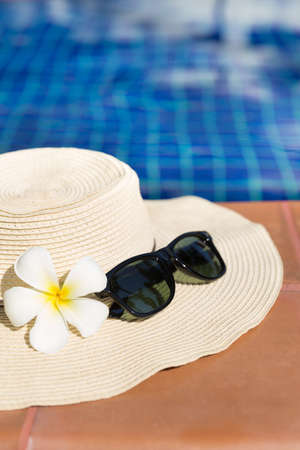 Sunglasses with flower and straw hat on border of a swimming pool - holiday tropical conceptの写真素材