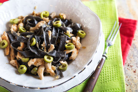 Black ink pasta with chicken breast and green olivesの写真素材