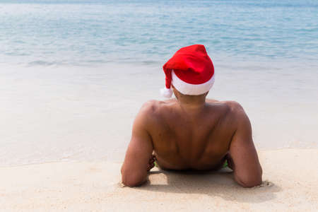 Man in Santa Claus red hat sits on the beach in morning hangover Christmas holiday party dreamsの写真素材
