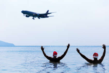 Two men in Santa Claus red hat greet salute airplane in morning hangover after Christmas holiday partyの写真素材