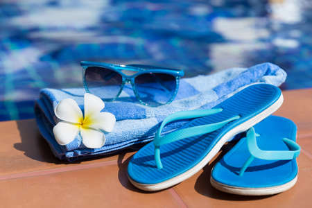 Blue slippers, sunglasses and towel on border of a swimming pool - holiday tropical conceptの写真素材
