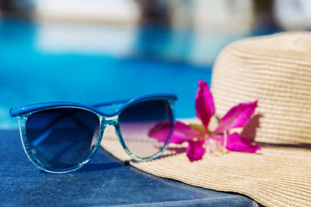 Sunglasses with flower and straw hat on border of a swimming pool - holiday tropical conceptの写真素材