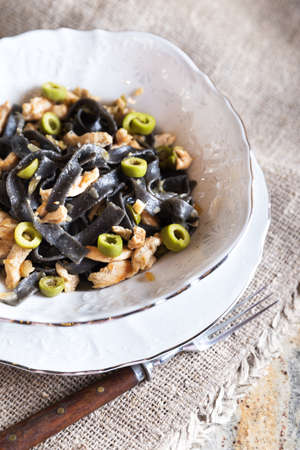 Black ink pasta with chicken breast and green olivesの写真素材