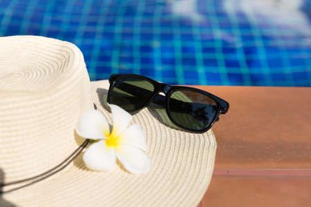 Sunglasses with flower and straw hat on border of a swimming pool - holiday tropical conceptの写真素材
