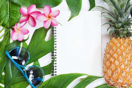 Tropical top view summer botanical concept still life notebook sunglasses pineapple frame with monstera liana, vine, palm leaves and plumeria frangipani flower flat lay layoutの写真素材