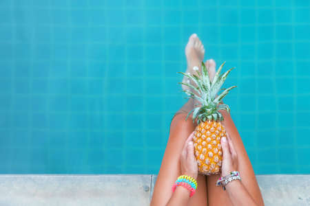 Slim woman holding pineapple fruit near swimming pool tropical exotic concept top viewの写真素材