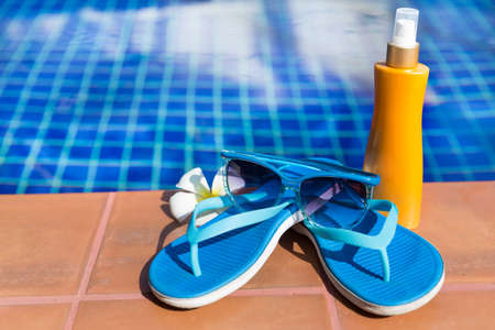 Blue slippers with sunscreen cream and sunglasses on border of a swimming pool - holiday tropical conceptの写真素材