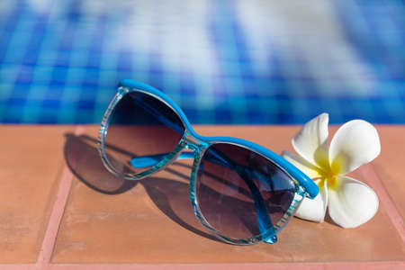 Blue sunglasses with  plumeria, frangipani flower on border of a swimming pool - holiday tropical conceptの写真素材