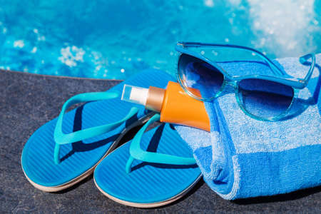 Sunglasses with sunscreen cream, blue slippers and towel on border of a swimming pool - holiday tropical conceptの写真素材