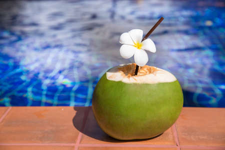 Fresh coconut juice with straw and plumeria, frangipani, flower on border of a swimming pool - holiday tropical conceptの写真素材