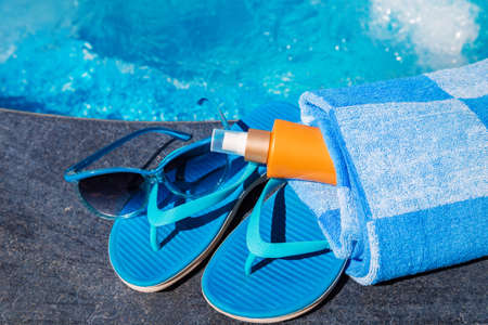 Sunglasses with sunscreen cream, blue slippers and towel on border of a swimming pool - holiday tropical conceptの写真素材