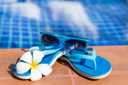 Blue slippers and sunglasses on border of a swimming pool - holiday tropical conceptの写真素材