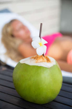 Coconut juice drink with woman on lounger near a swimming pool - holiday tropical conceptの写真素材