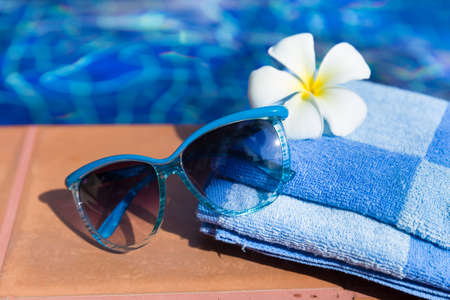 Fluffy towel with sunglasses and flower on border of a swimming pool - holiday tropical conceptの写真素材