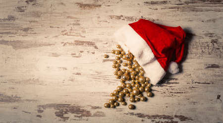 Christmas composition with Santa hat full of golden sparkling baubles on wooden background holiday conceptの写真素材