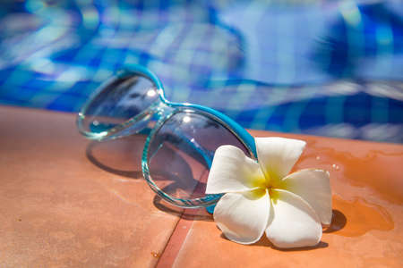 Blue sunglasses with  plumeria, frangipani flower on border of a swimming pool - holiday tropical conceptの写真素材