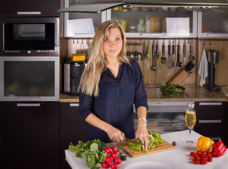 Young pretty blond young woman cooking salad in the kitchenの写真素材
