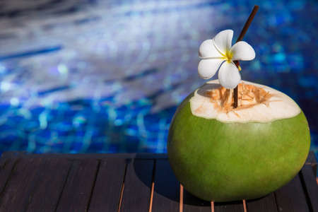 Fresh coconut juice with straw and plumeria, frangipani, flower on border of a swimming pool - holiday tropical conceptの写真素材