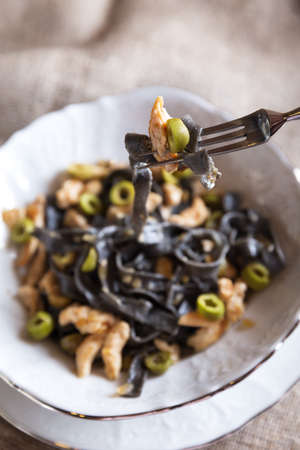 Black ink pasta with chicken breast and green olivesの写真素材