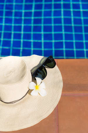 Sunglasses with flower and straw hat on border of a swimming pool - holiday tropical conceptの写真素材