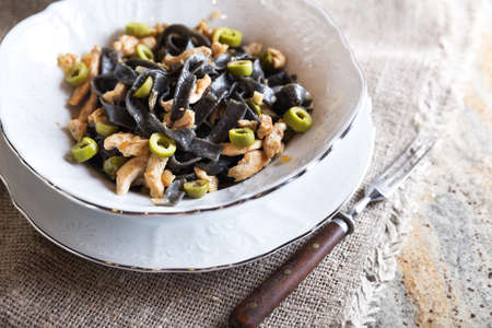 Black ink pasta with chicken breast and green olivesの写真素材