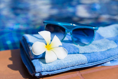 Fluffy towel with sunglasses and flower on border of a swimming pool - holiday tropical conceptの写真素材