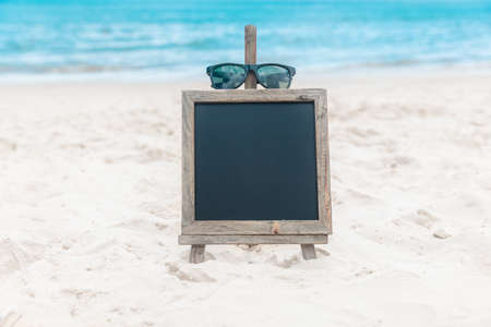 Chalk board with sunglasses on the sea beach sand summer tropical holiday conceptの写真素材