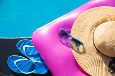 Blue slippers, sunglasses, straw hat and pink air mattress on border of a swimming pool - holiday tropical conceptの写真素材