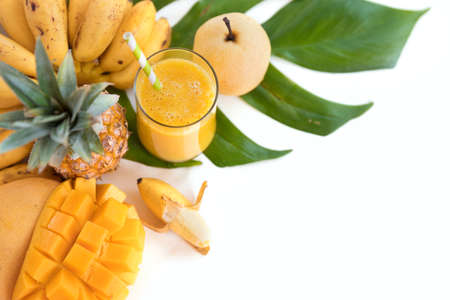 Tropic flat lay top view summer concept with yellow tropical banana mango pineapple pear fruits and smoothie juice palm leaves and plumeria on whiteの写真素材