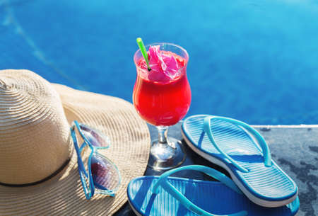 Watermelon fresh juice smoothie drink glass with flower, sunglasses, slippers and straw hat on border of a swimming pool - holiday tropical conceptの写真素材