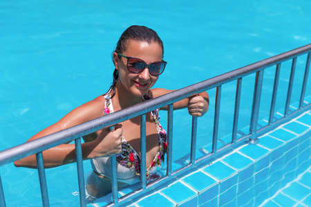 beautiful young slim brunette woman in sunglasses sunbathe in the swimming poolの写真素材